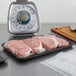 A CKF black foam meat tray with raw meat on a counter.