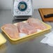 A yellow CKF foam tray holding two raw chicken breasts on a counter.