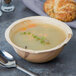 A TreeVive by EcoChoice palm leaf bowl filled with soup with a spoon and a piece of bread.