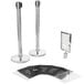 A group of Lancaster Table & Seating stainless steel crowd control stanchions with clear signs on top.