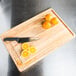 A Tablecraft wood cutting board with oranges cut in half on it.