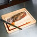 A piece of meat being cut on a Tablecraft wood cutting board.