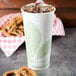 A white Bare by Solo paper cold cup with a green leaf design filled with ice tea and pretzels.