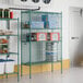 A green metal Regency wire security cage with shelves holding food items.