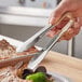 A person using Vollrath stainless steel tongs with tan Kool-Touch handles to serve food.