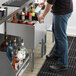 A man using a Regency underbar ice bin to fill a glass with ice.