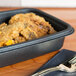A black tray from Genpak with food in it and a fork on a napkin.