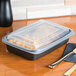A black Genpak rectangular plastic container with food inside on a table.