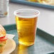 A translucent plastic cup filled with a drink next to a sandwich on a tray.