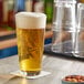 A Libbey stackable mixing glass of beer on a table with foam on top.