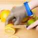 A person using a San Jamar stainless steel mesh glove to cut a lemon.