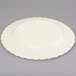 A Fineline Flairware ivory plastic plate with a wavy design on a gray surface.