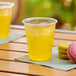 A Choice translucent plastic cup filled with yellow liquid next to pink and yellow macaroons.