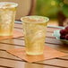 Two Choice translucent plastic cups filled with ice and liquid on a table.