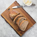 A Tablecraft acacia wood rectangular serving board with sliced bread and butter next to a knife.