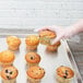 A person in gloves holding a Chicago Metallic bakery display tray with a blueberry muffin in a wrapper.