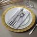 A white plate with a gold geometric design on the rim with silverware on a white napkin.