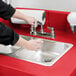 A person washing their hands in a red Cambro CamKiosk hand sink.