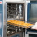 A woman using a Rational CombiFry tray to cook french fries in an oven.