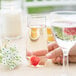 A hand holding a WNA Comet clear plastic stemless flute with water and a raspberry in it.