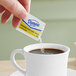 A hand holding a Domino sugar packet over a cup of coffee.