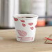 A close-up of a EcoChoice paper hot cup of coffee with red leaves on it.
