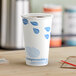 A close-up of a white EcoChoice paper hot cup with blue leaves on it.