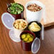 A Carlisle black plastic crock with lid on a table with salad, pickles, lemon slices, and croutons.