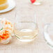 A clear plastic stemless wine goblet filled with white wine on a table next to a yellow and white pastry.
