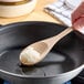 A person using a wooden spoon to stir white coconut oil in a pan.