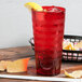 A red Orbis plastic tumbler filled with red liquid on a table with chips and salsa.