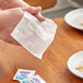 A hand holding a white Purell hand sanitizing wipe over a table of food.