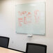 A white Aarco Pure Glass Marker Board with red marker drawings on it.