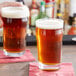 Two Acopa English Pub glasses of beer on a bar counter.