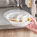 A hand holding a Choice white plastic microwavable container with food inside.