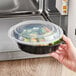 A hand holding a Choice black plastic microwavable container filled with food.