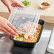 A person's hands holding a black rectangular Choice plastic container filled with food.