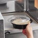 A hand holding a black Choice plastic container of food in a microwave.