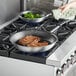 A woman cooking meat in a Vollrath Wear-Ever non-stick fry pan on a stove.