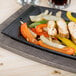 A Lodge rectangular cast iron fajita skillet with chicken, peppers and onions on a table.