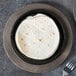 A tortilla on a plate next to a Lodge cast iron fajita skillet with a fork.