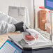 A person in black gloves weighing meat on a scale using a Choice Deli Saddle Bag.