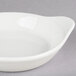 A CAC bone white stoneware shirred egg dish with a handle on a gray surface.