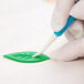 A hand using a blue and white Ateco sculpturing tool to paint a green leaf.