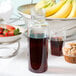 A Cal-Mil polycarbonate bottle filled with liquid on a table with a bowl of strawberries and muffins.