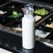 A Cal-Mil polycarbonate salad dressing bottle with a blue lid filled with white liquid on a counter.