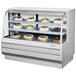 A white Turbo Air refrigerated bakery display case with cakes and pastries on curved glass shelves.