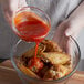 A person pouring Crystal hot sauce into a bowl of chicken wings.