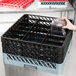 A hand holding a clear glass in a black and grey plastic crate.