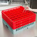 A hand holding a glass over a stack of red and gray plastic Noble Products glass racks.